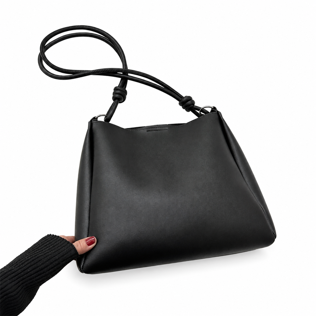 Black shoulder bag with slim knotted straps and metal rings, held by the original hand on a white background.