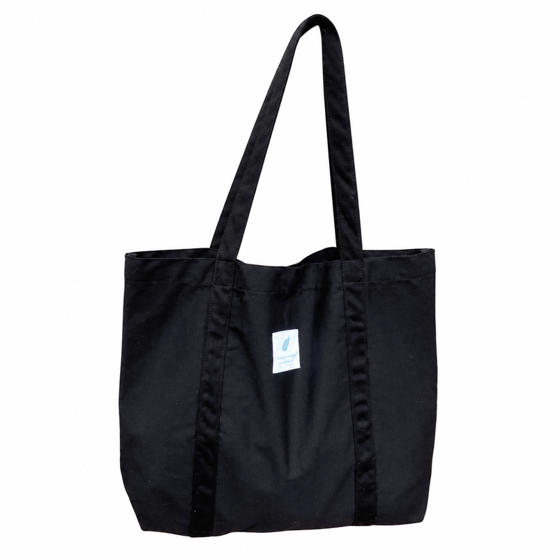 Black canvas tote with long fabric handles and original white sewn label on a white background.